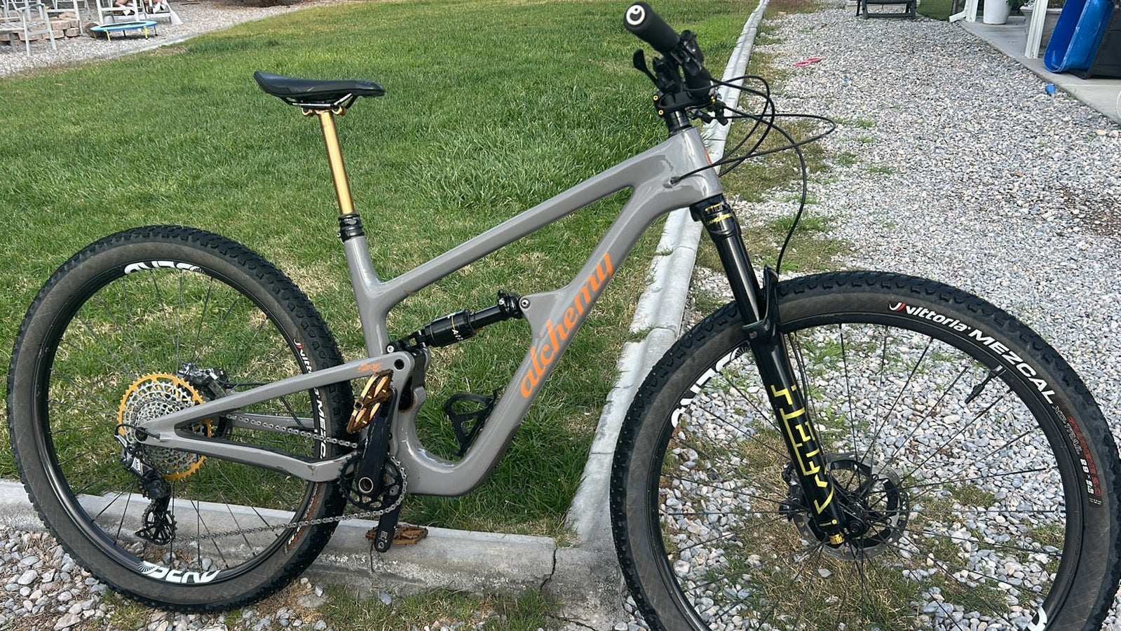 Gray mountain bike on a gravel path with grass and a building in the background